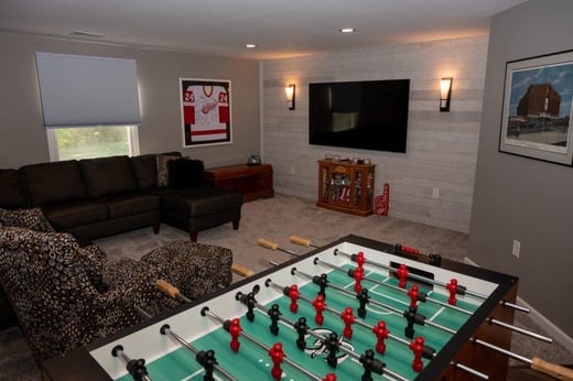 Finished basement living room with can lighting in ceiling and wall mounted lights on shiplap accent wall