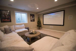 finished basement with white sofa and a projection screen on the wall showing a movie
