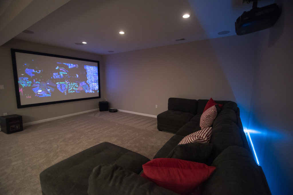 movie theater room in basement with large sectional and projection tv