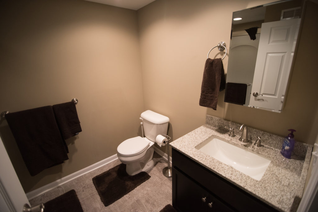 vinyl tile in basement bathroom with beige colored walls and granite countertop on vanity
