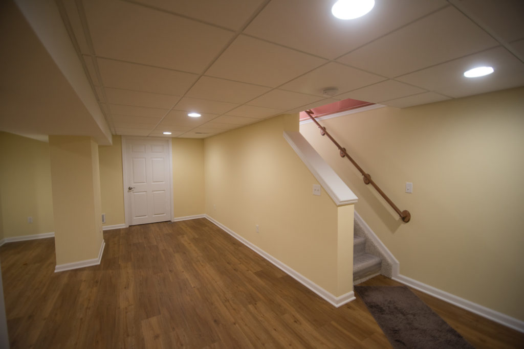 Bright yellow basement with open view staircase and vinyl plank flooring
