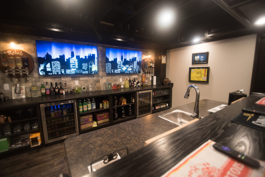 basement bar with dual tv screens and island with seating