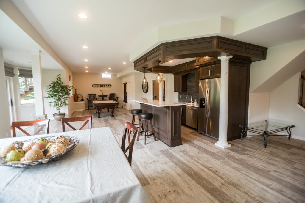 open floorplan basement with bar in the middle with soffit and dark stain