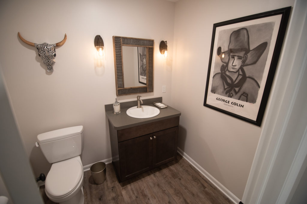 finished basement bathroom with brown vanity and light brown vinyl plank flooring and sconce lighting