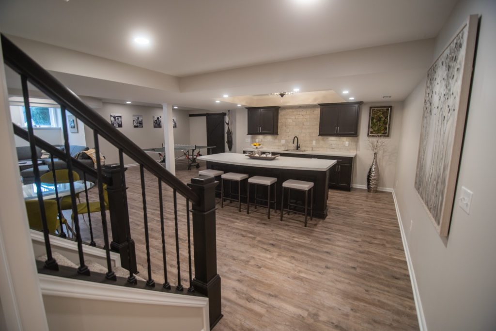 open rail basement staircase with brown vinyl plank flooring and bar