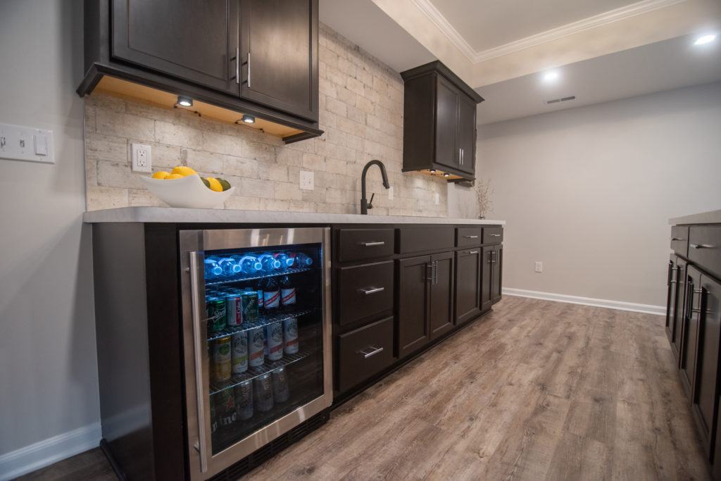 finished bar area in basement with dark brown cabinetry and light brown vinyl plank flooring, under cabinet lighting