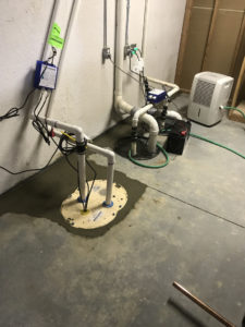 A sump pump and dehumidifier installed in a basement.