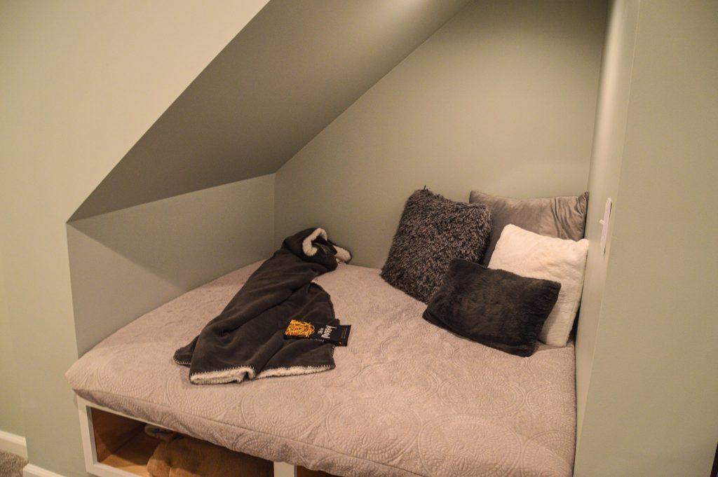 Finished basement reading nook built underneath the stairs with blankets and pillows for comfort reading.