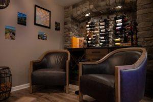 Renovated basement with lounge area featuring large chairs and a bar area behind them