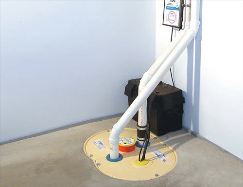 TripleSafe sump pump installation by Basements Plus. White PVC pipes running from a basin with battery backup.