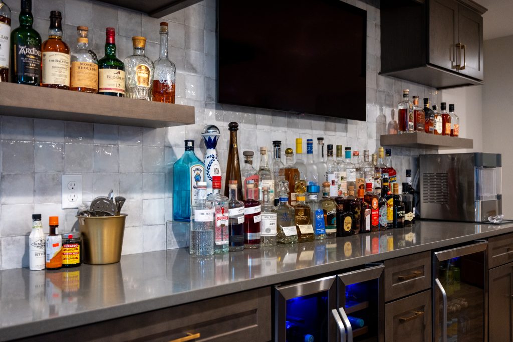 Oakland Township. Basements Plus remodeled basement showing alcohol lining the walls of a dark wood bar and mounted TV.