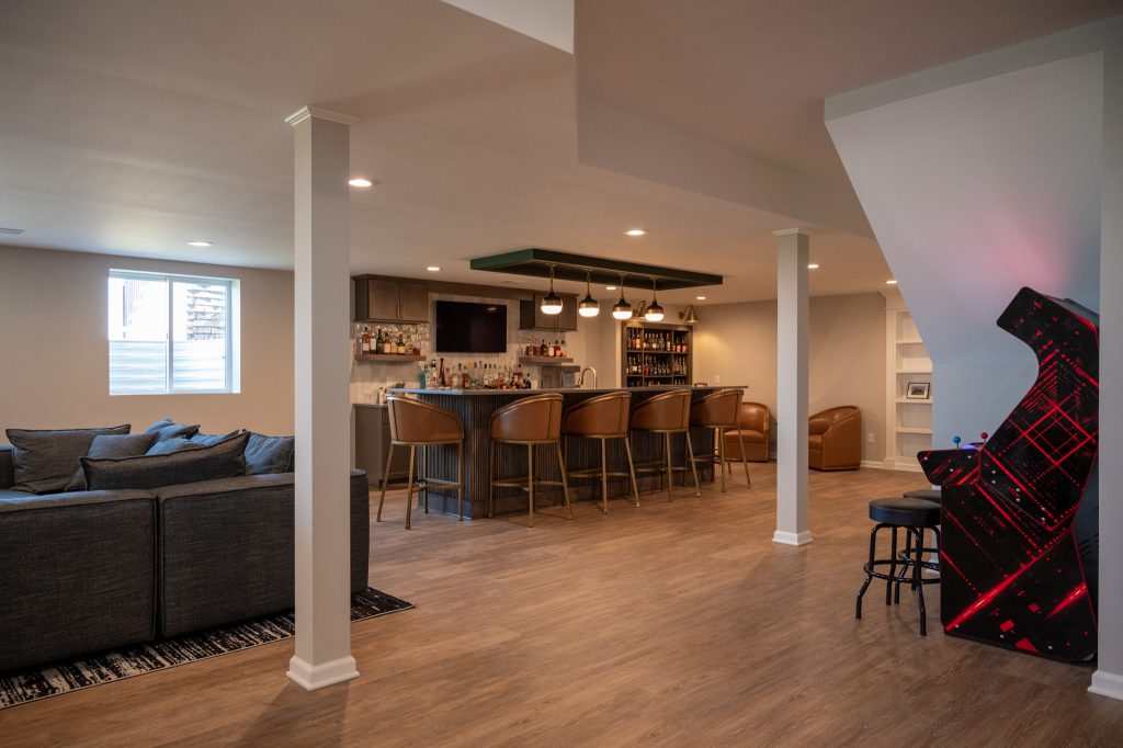 Finished basement featuring brown hardwood flooring, exposed support beams, and newly installed bar