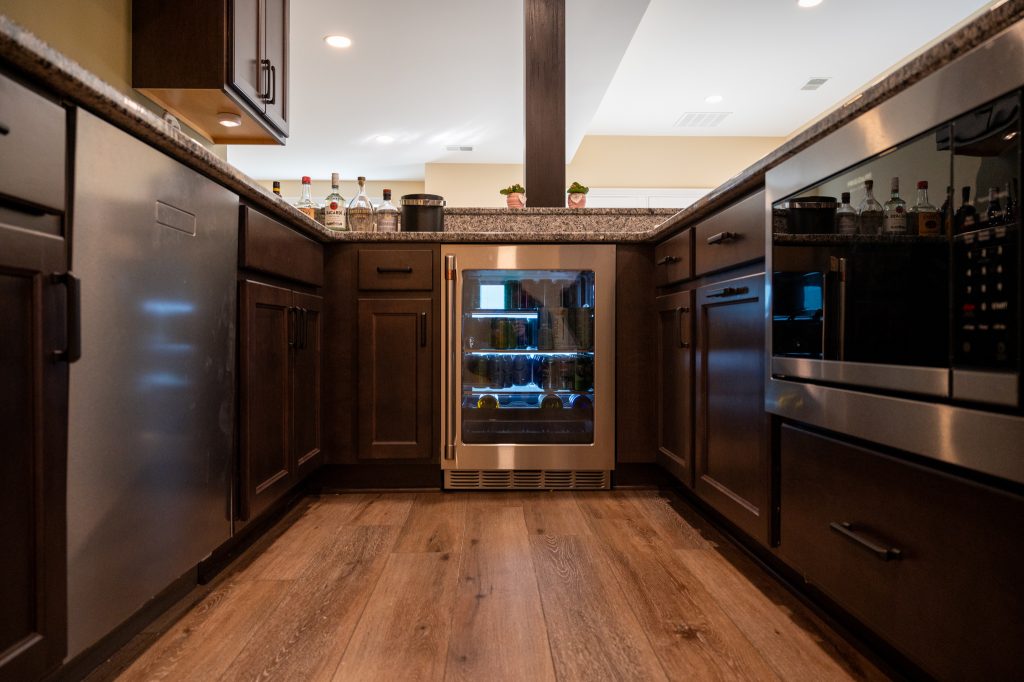 Mini cooler in finished basement with brown cabinets and hardwood flooring