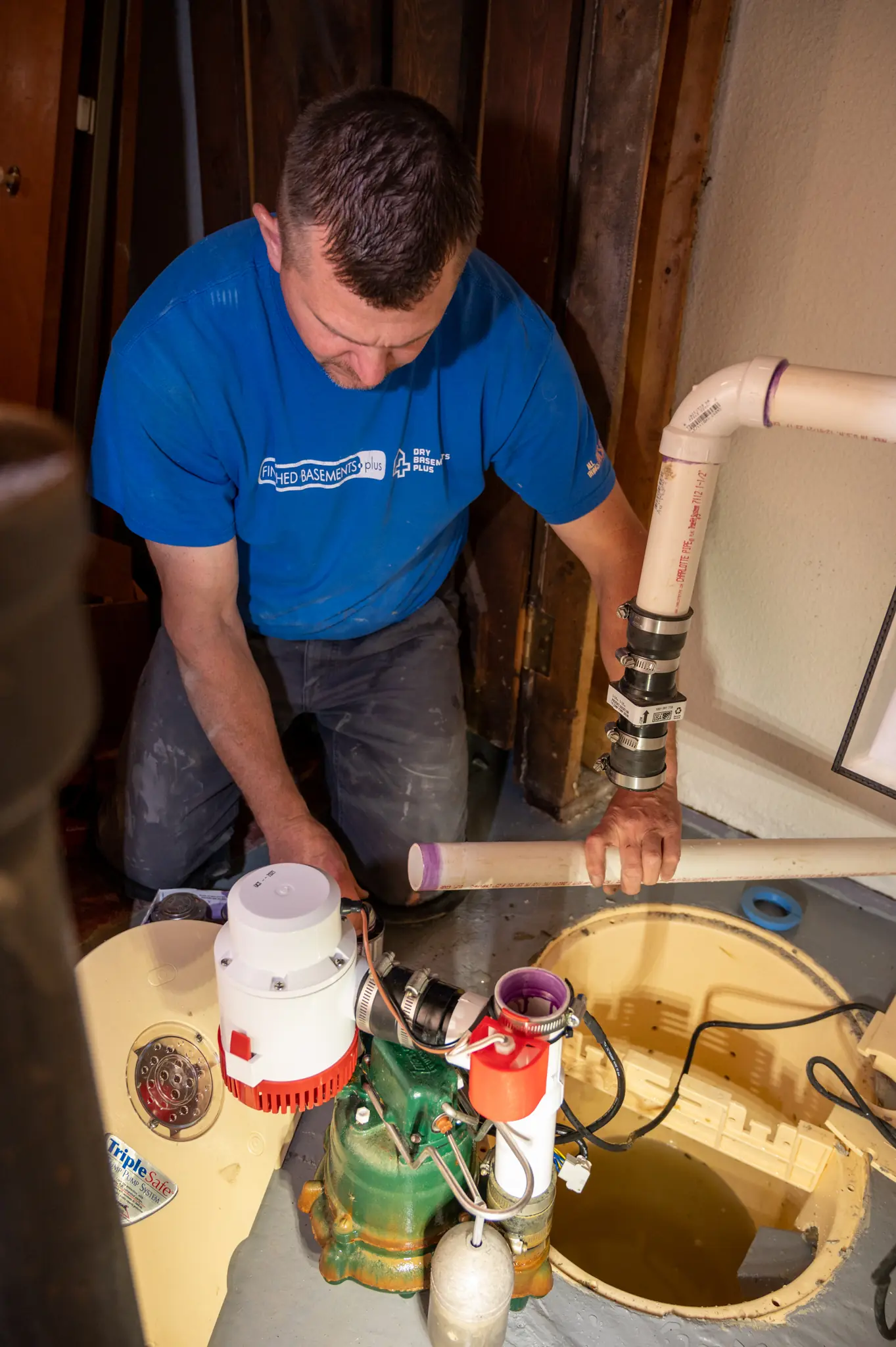 Photo of Basements Plus crew member working on the plumbing while installing a sump pump.