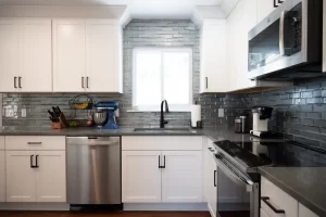 Photo of remodled kitchen in Ann Arbor, Michigan with white cabinetry and dark backsplash and appliances.