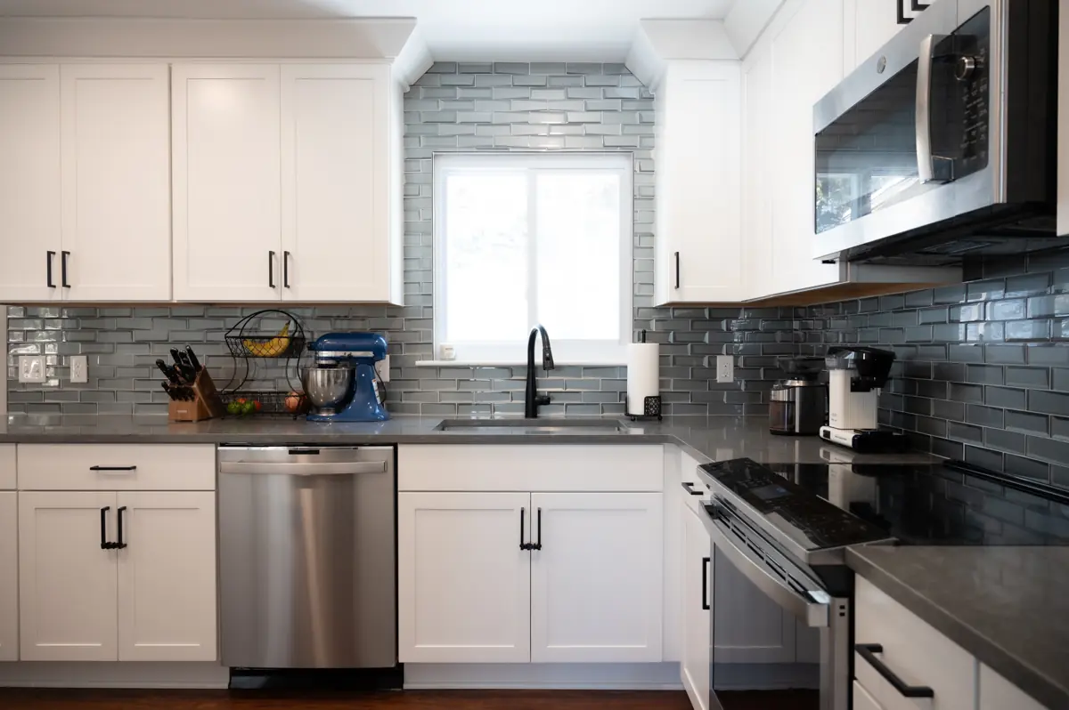 Photo of remodled kitchen in Ann Arbor, Michigan with white cabinetry and dark backsplash and appliances.