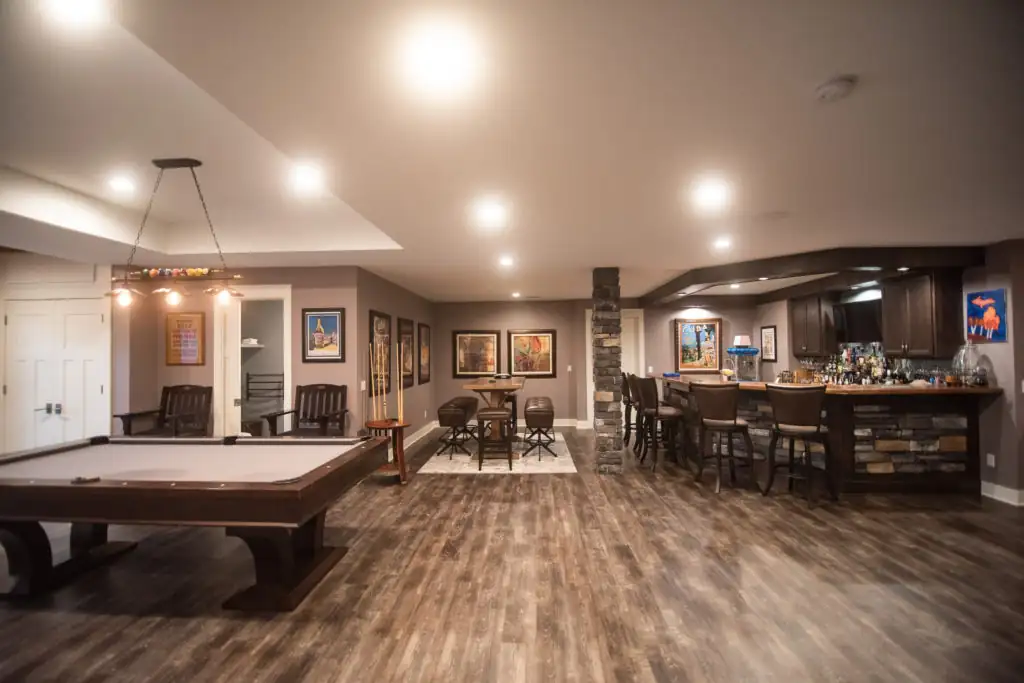 Finished basement with brown and beige tone with bar and pool table.